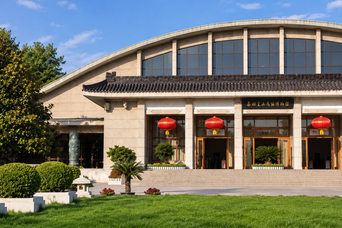 弧形屋顶下的遗址入口：一号坑保护大厅的弧形屋顶与前部灰瓦门廊形成两层轮廓，树木、绿地与通道共同提示原址大厅的尺度。